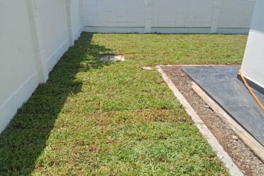 A rectangular section of a residential yard covered with recently laid turf grass (sod), bordered by a patio and white brick walls.
